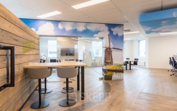 Bright, modern workspace with a wooden accent wall, high chairs, stylish flooring, and large windows at Costerweg 5, Veghel, ideal for office space rental.