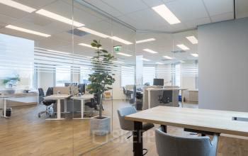 Modern office space at Costerweg 5, Veghel, featuring glass walls, wooden floors, and contemporary furnishings ideal for collaborative workspaces. Available for office space rental.