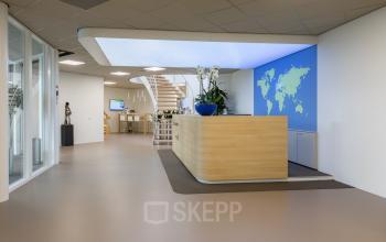 Modern office entrance at Costerweg 5, Veghel featuring a sleek reception desk, illuminated ceiling, and world map wall art. Ideal for office space rental, the design is contemporary and professional.