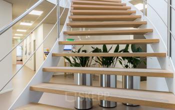 Modern office interior at Costerweg 5, Veghel featuring a curved stairway with wooden steps and metal railings, leading to a bright upper floor. Ideal for office space rental.