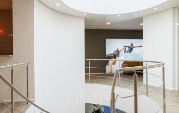 Modern office interior at Costerweg 5, Veghel, featuring stylish wooden flooring and a spiral staircase beneath a skylight, perfect for businesses seeking office space rental.
