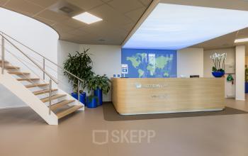 Modern reception area with a sleek wooden desk, world map display, and potted plants at Costerweg 5, Veghel. Ideal for office space rental.