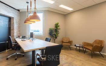 Modern workspace at Costerweg 5 in Veghel featuring a wooden table, black chairs, brown armchairs, and stylish pendant lights, ideal for office space rental.