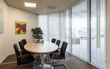 Bright conference room at Costerweg 5, Veghel, featuring a round table with black chairs, decorated with a colorful butterfly painting and indoor plant. Ideal office space rental for meetings.