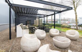Outdoor seating area at Gildestraat 13 in Velp, ideal for office space rental with a mix of modern benches and sculptural chairs beneath a sleek pergola.