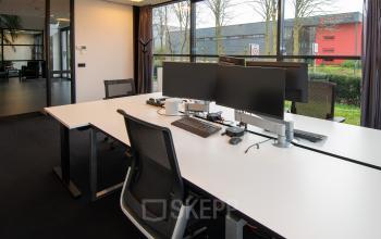 Modern office space at Gildestraat 13, Velp, featuring a sleek workspace with multiple monitors and large windows overlooking greenery, available for office space rental.