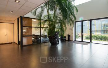 Spacious office entrance at Gildestraat 13, Velp, with a large plant and visible conference room, ideal for office space rental.