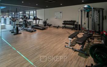 Modern fitness area available for office space rental at Gildestraat 13, Velp, featuring exercise equipment and mirrored walls for an invigorating work environment.