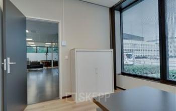Interior view of a furnished office space at Noorderpoort 43, Venlo, featuring a desk, cabinet, and large windows offering natural light—ideal for office space rental.