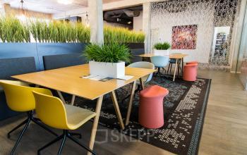 Modern office space rental with stylish furnishings, including wooden tables, colorful chairs, and decorative plants, available at Kaldenkerkerweg 20 in Venlo.