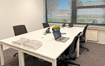 Bright office space at Noorderpoort 33 33, Venlo, featuring a large table with office chairs, telephones, and a laptop, ideal for office space rental. Natural light from large windows adds a welcoming touch.
