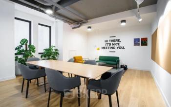 Modern workspace in Venlo featuring a sleek wooden table, comfortable chairs, greenery, and minimalist art. The room has a welcoming vibe, perfect for office space rental meetings.