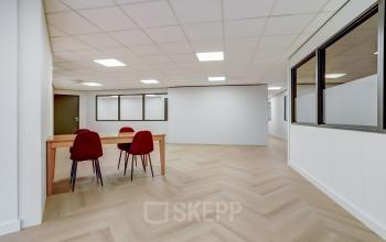 Interior view of a modern office space at Keizersveld 47, Venray, showcasing a well-lit open floor plan with wooden flooring. The office space rental offers a minimalist setup with chairs around a wooden table.