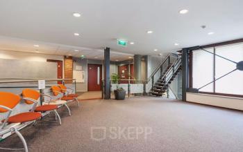 Interior of office building at Kennedyplein 18, Venray, featuring a spacious open area with seating and a staircase.