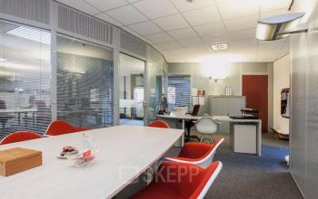 Modern office interior at Kennedyplein 18, Venray with a large table, red chairs, and workspaces in the background, ideal for office space rental.
