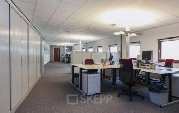 Modern office space rental at Kennedyplein 18, Venray, featuring spacious desks, chairs, and computer equipment in a well-lit room with multiple windows.