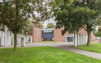 Exterior view of the office building at Kennedyplein 18, Venray, surrounded by green lawn and trees.