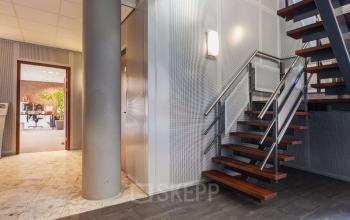 Modern office entrance with sleek metal stairs and a view into workspaces at Kennedyplein 18, Venray, ideal for office space rental.