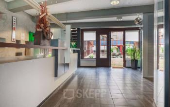 Modern office entrance with tiled floor, reception desk, and large windows at Kennedyplein 18, Venray. Ideal for office space rental.