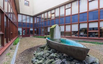 View of the courtyard at Kennedyplein 18, Venray with modern office building featuring large windows and a unique boat sculpture centerpiece.