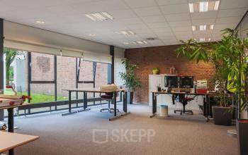 Spacious, bright office space rental at Kennedyplein 18, Venray with large windows, plants, and desks with computers.