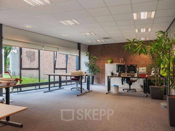 Spacious, bright office space rental at Kennedyplein 18, Venray with large windows, plants, and desks with computers.