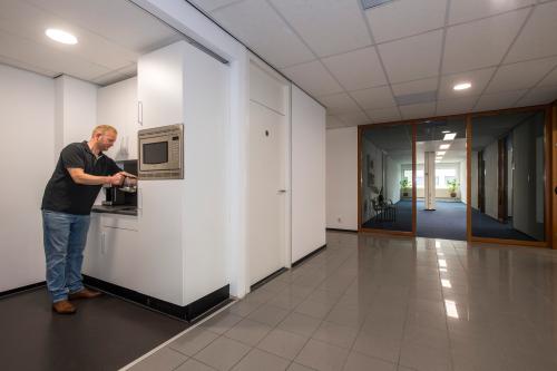 A professionally dressed man prepares coffee in a pantry area of an office space rental at Witboom 1, Vianen Utr.