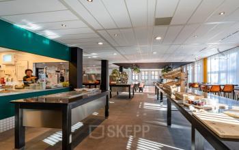 Spacious pantry area at Lange Dreef 17, Vianen Utr, featuring sleek countertops and modern lighting with people engaging in culinary activities. Ideal for office space rental with vibrant and functional design.