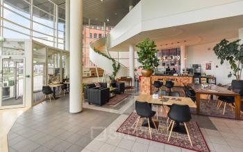 Spacious office lounge at Regulusweg 11, Voorburg featuring modern furniture for rent office space with a relaxed seating area and coffee bar. Numerous plants enhance the inviting atmosphere.