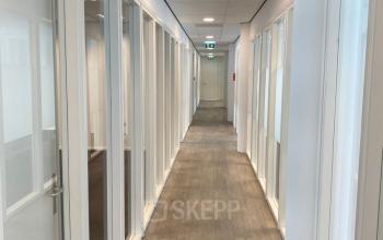 A long hallway with glass doors on both sides in an office building at Regulusweg 11, Voorburg. Natural light illuminates the hallway, suggesting potential office space rentals for private offices.