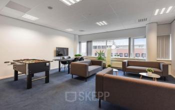 Modern furnished office space for rent at Regulusweg 11, Voorburg, featuring a foosball table, seating area, and large windows.