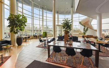 Spacious, modern office interior with large windows and tables, ideal for office space rental at Regulusweg 11, Voorburg.