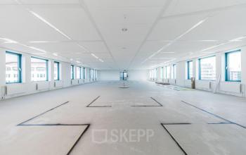 Spacious office space with large windows and empty floor, ideal for office space rental in Voorburg.