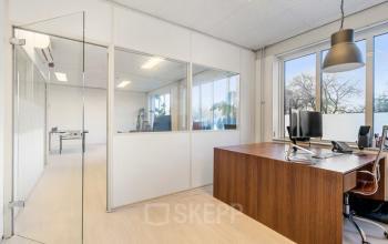 Spacious office to rent at Agro Business Park 22, Wageningen, featuring large windows, a wooden desk, and a computer setup. Ideal for office space rental with an abundance of natural light.