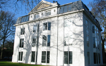 Exterior view of the office building located at Van der Oudermeulenlaan 1, Wassenaar, featuring large windows and a manicured lawn. Ideal for office space rental.