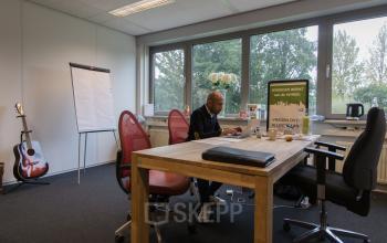 Contemporary office space rental at Houttuinlaan 4, Woerden, with a focused individual working at a desk surrounded by modern furnishings and a flip chart.