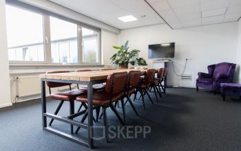 Modern Woerden office space rental at Houttuinlaan 4 featuring a large table with chairs and a cozy seating area with a purple couch.