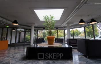 Modern office space rental at Houttuinlaan 4, Woerden, featuring lounge area with comfortable seating and greenery under a skylight.