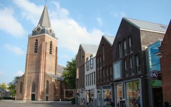 Exterior view of office building at Pelmolenlaan 17A, Woerden, situated adjacent to a church with a tall tower, showing commercial units on the ground floor.