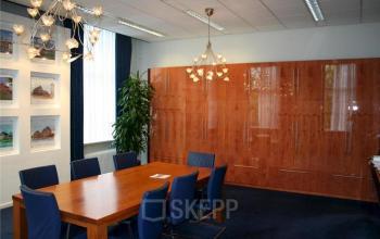 Modern office space with wooden table, blue chairs, and cabinetry at Westdam 3D, Woerden. Elegantly furnished with artwork and plants, perfect for office space rental.
