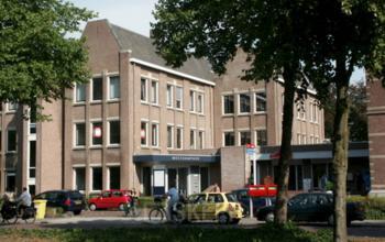 Exterior view of office building at Westdam 3D, Woerden, featuring multiple brick facades, parked cars, and pedestrians on the sidewalk.