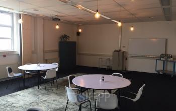 Spacious Woerden office space rental at Korenmolenlaan 4 with round tables and comfortable seating under warm lighting.