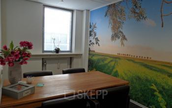 Bright conference room at Pompmolenlaan 18 in Woerden with a large wooden table, black chairs, and a wall mural of a green field, ideal for office space rental.