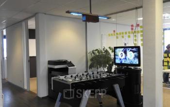 Office with a foosball table, TV displaying a sports score, and office equipment at Pompmolenlaan 9, Woerden, available for rent.