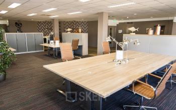 Modern office space with wooden desks, brown leather chairs, and decorative elements located at Zaagmolenlaan 4 in Woerden, ideal for office space rental.
