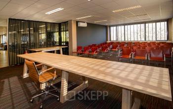 Professional meeting room at Zaagmolenlaan 4, Woerden, with rows of red chairs, large windows, and multiple tables.
