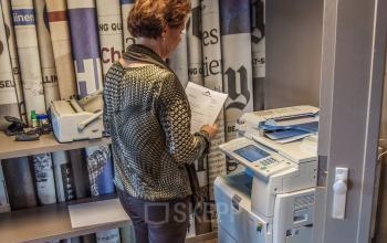 Person operating a copier in a small office space with shelves at Zaagmolenlaan 4, Woerden. Ideal office space rental for efficient work.
