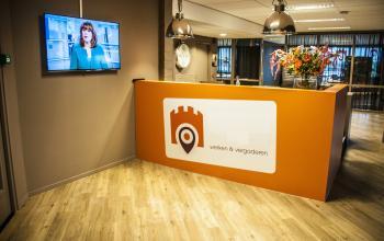 The reception area at Zaagmolenlaan 4, Woerden, featuring a bright orange desk, floral arrangement, and a wall-mounted TV.