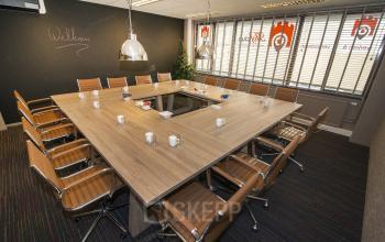 Modern conference room at Zaagmolenlaan 4, Woerden, with wooden tables arranged in a U-shape, brown leather chairs, and large windows. Ideal office space rental for professional meetings.