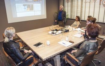 Business meeting room in the office at Zaagmolenlaan 4, Woerden, with professionals engaged in a presentation around a large wooden table.